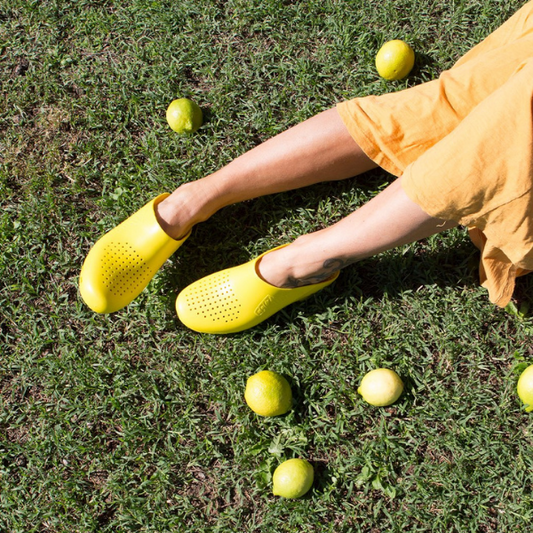 Woman wearing Yellow Calzuro Classics with Holes laying in the grass next to lemons in a yellow sundress