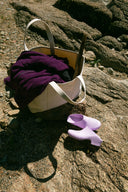 classic lavender with holes clogs on rock next to cream bag with purple jacket coming out of the top