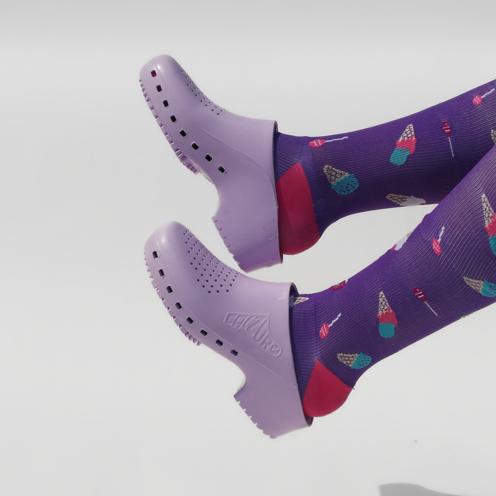 Purple socks with colorful designs worn with matching purple calzuro clogs on a light gray background