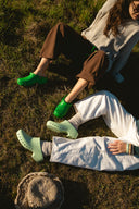 Two people sitting on the grass wearing green Calzuro shoes.